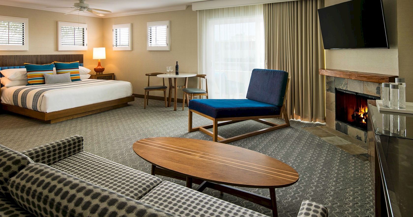 A spacious hotel room with a bed, seating area, fireplace, TV, and a round coffee table&mdash;cozy, modern, and neatly arranged.