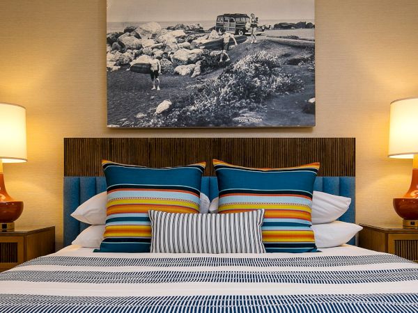 A neatly made bed with striped pillows, blue headboard, two wooden nightstands, lamps, and a black-and-white landscape photo above the headboard.