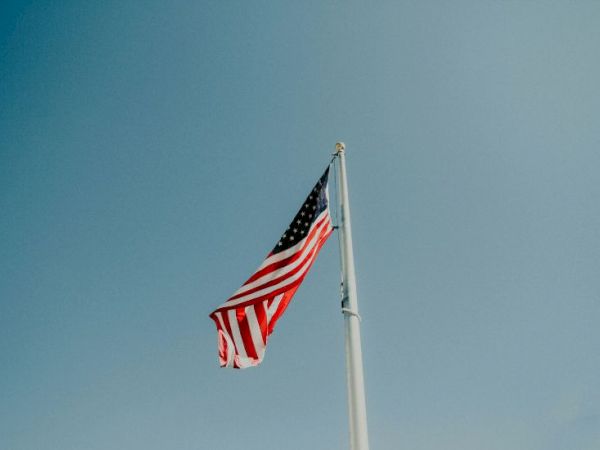 A waving American flag on a tall flagpole against a clear blue sky.