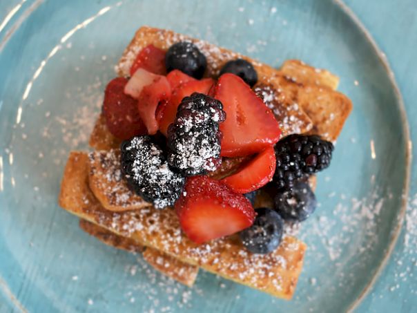 Delicious-looking waffles topped with fresh berries&mdash;strawberries and blueberries&mdash;dusted with powdered sugar on a blue plate.