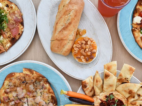 A colorful pizza and bread feast on blue plates with dips and a fresh green salad nearby. End.