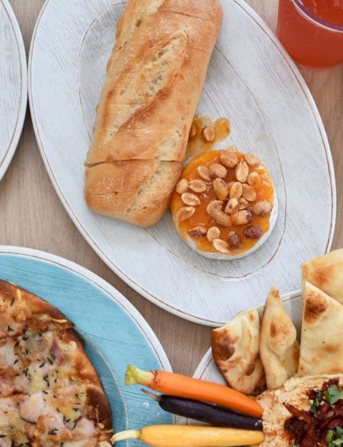 Assorted pizzas, a garlic bread baguette, breadsticks, tortilla chips with salsa, a veggie platter, and drinks on a shared feast table.