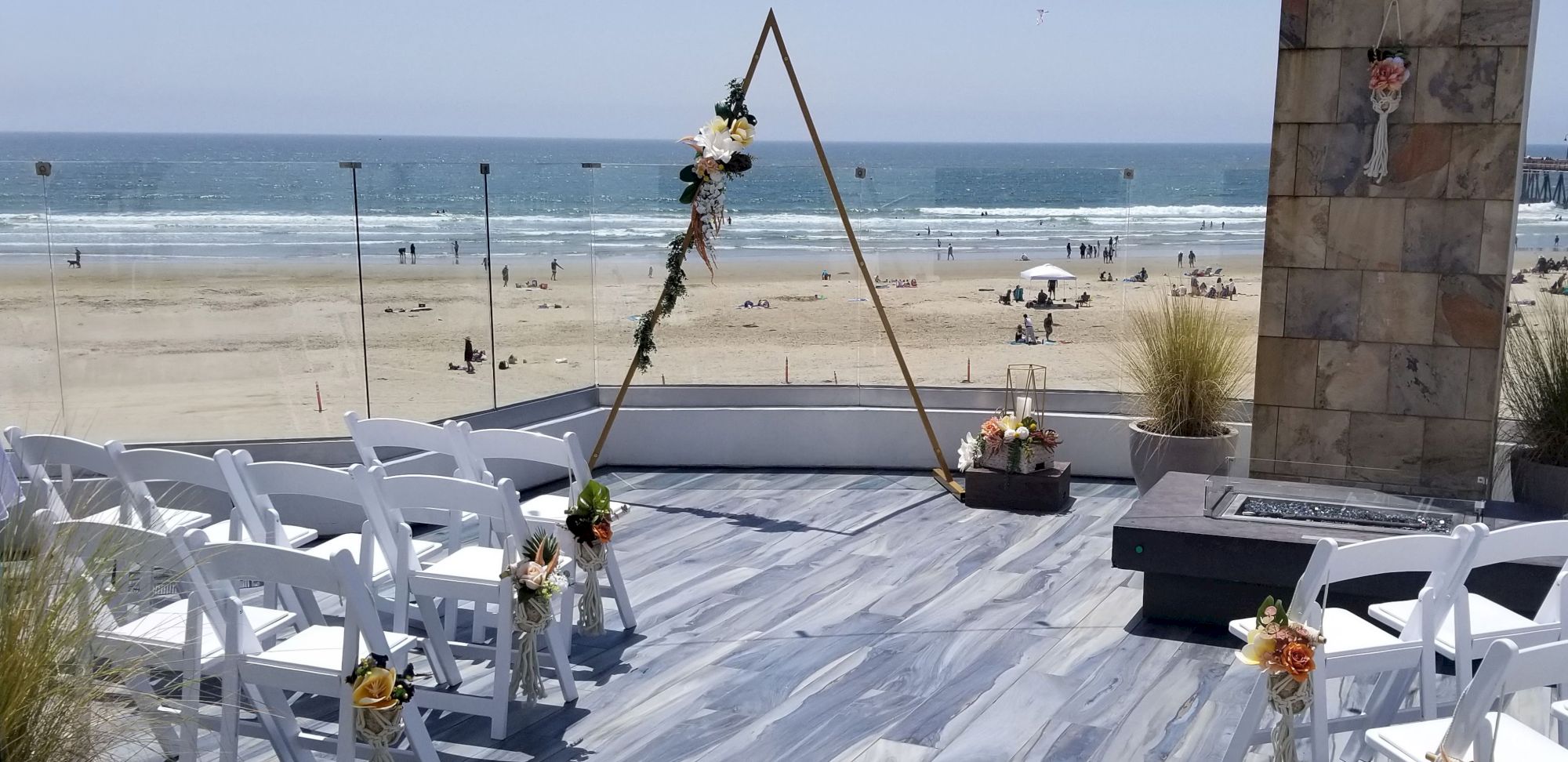 A beach wedding setup with a wooden arch, white chairs, floral decor, and a view of the sandy shore and ocean beyond.