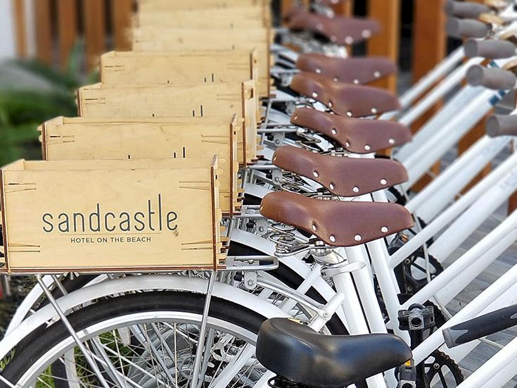 Row of identical bikes with brown saddles, lined up with wooden sandcastle branded baskets at the front, ready for rides.
