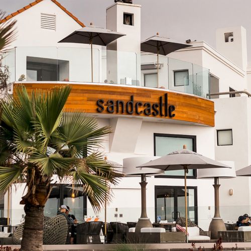 A white two-story Mediterranean house with a tiled roof, arched windows, balcony, and a small palm tree in front.