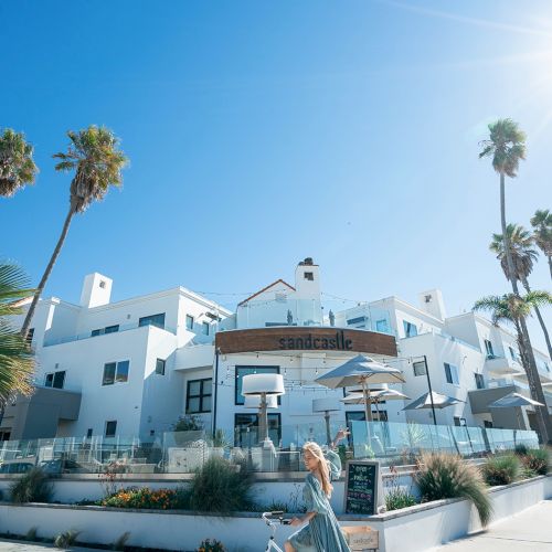 A sunny street scene with a blue house, palm trees, and a bicycle leaning against a fence under a clear sky.