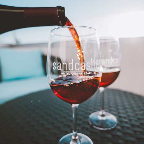 Red wine is poured into two glasses on a table, bottle pouring from left, label reads &ldquo;sandcastle.&rdquo;
