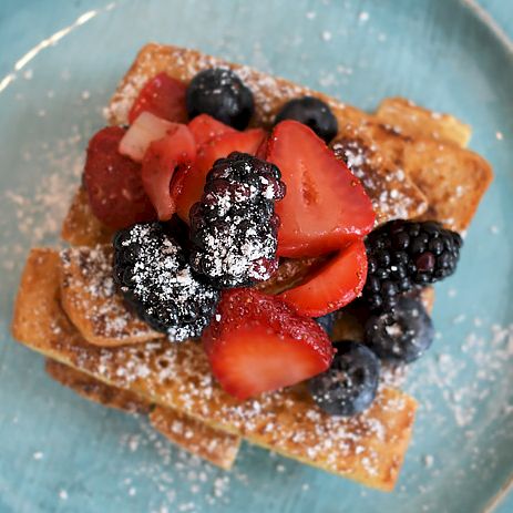 A plate of waffles topped with fresh berries (strawberries, blueberries) and a dusting of powdered sugar, on a turquoise plate.