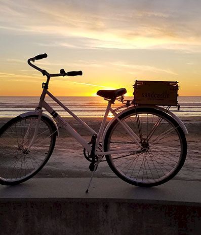 A bicycle parked on a sunlit beach at sunset, silhouette against a golden sky by the waves.
