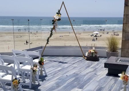 A wooden pier with a rope swing, a chair, and seagulls near the boards; ocean and beach visible in the background, sunny day.
