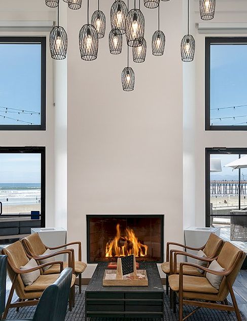 Cozy modern lounge with a fireplace, mid-century chairs, glass pendant lights, and large ocean-view windows F- zoomed.